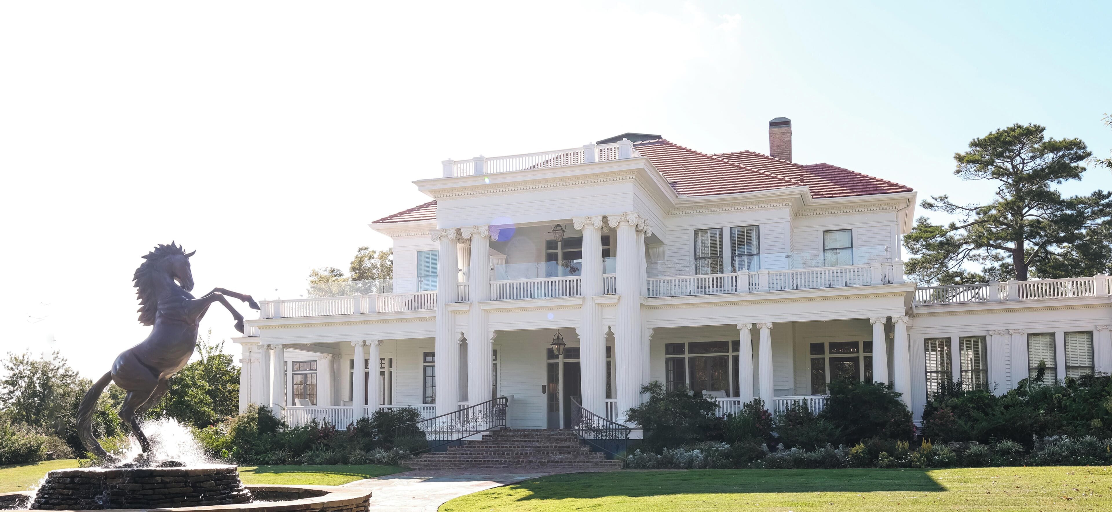 A large white building with a red roof, multiple balconies, and a statue of a horse.