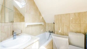 A bathroom with a skylight, a bathtub, and a toilet. - 2-Bed Loft Apartment for 5ppl with private parking (Beckenham)