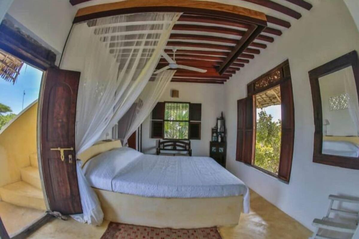 A bedroom with a bed, a wooden ceiling, a window, and a door.