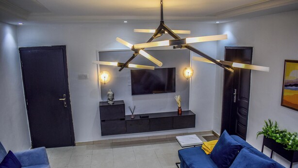 Un salon moderne avec un canapé bleu, un meuble de rangement noir pour appareils électroniques et un luminaire suspendu au plafond.
