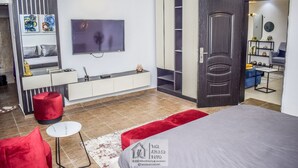 Une chambre moderne avec un lit, une télévision, une armoire et un pouf rouge.