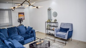 Un salon moderne avec un canapé bleu, un fauteuil gris, une table basse et un luminaire au plafond original.