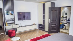 A modern bedroom with a bed, a TV, a wardrobe, and a red ottoman. - Beautiful One Bed Apartment in Lekki Phase1 (Lagos)