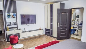 Ein modernes Schlafzimmer mit einem Bett, einem Fernseher, einem Kleiderschrank und einem roten Hocker.