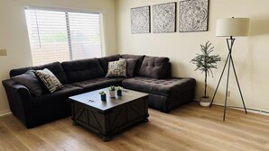 A living room with a sectional sofa, a coffee table, a floor lamp, and a potted plant.