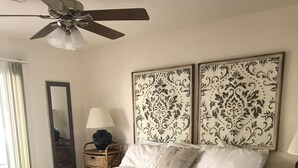 A bedroom with a large bed, two nightstands, a ceiling fan, and decorative wall panels.