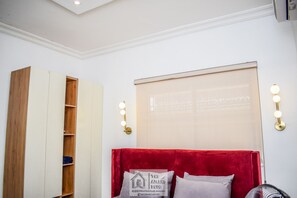 Un dormitorio con cabecera roja, un armario de madera y un aplique de pared.