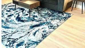 Un salon moderne avec un canapé d’angle gris, une table basse en bois et un tableau abstrait aux couleurs bleue et blanche accroché au mur.