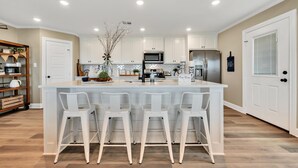 A modern kitchen with a central island, white bar stools, and a built-in microwave. - Farmhouse Charm - Waco/Magnolia/Baylor (Waco)