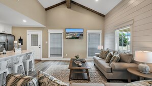 A spacious living room with a high ceiling, a kitchen area, and a large window with blinds. - Farmhouse Charm - Waco/Magnolia/Baylor (Waco)