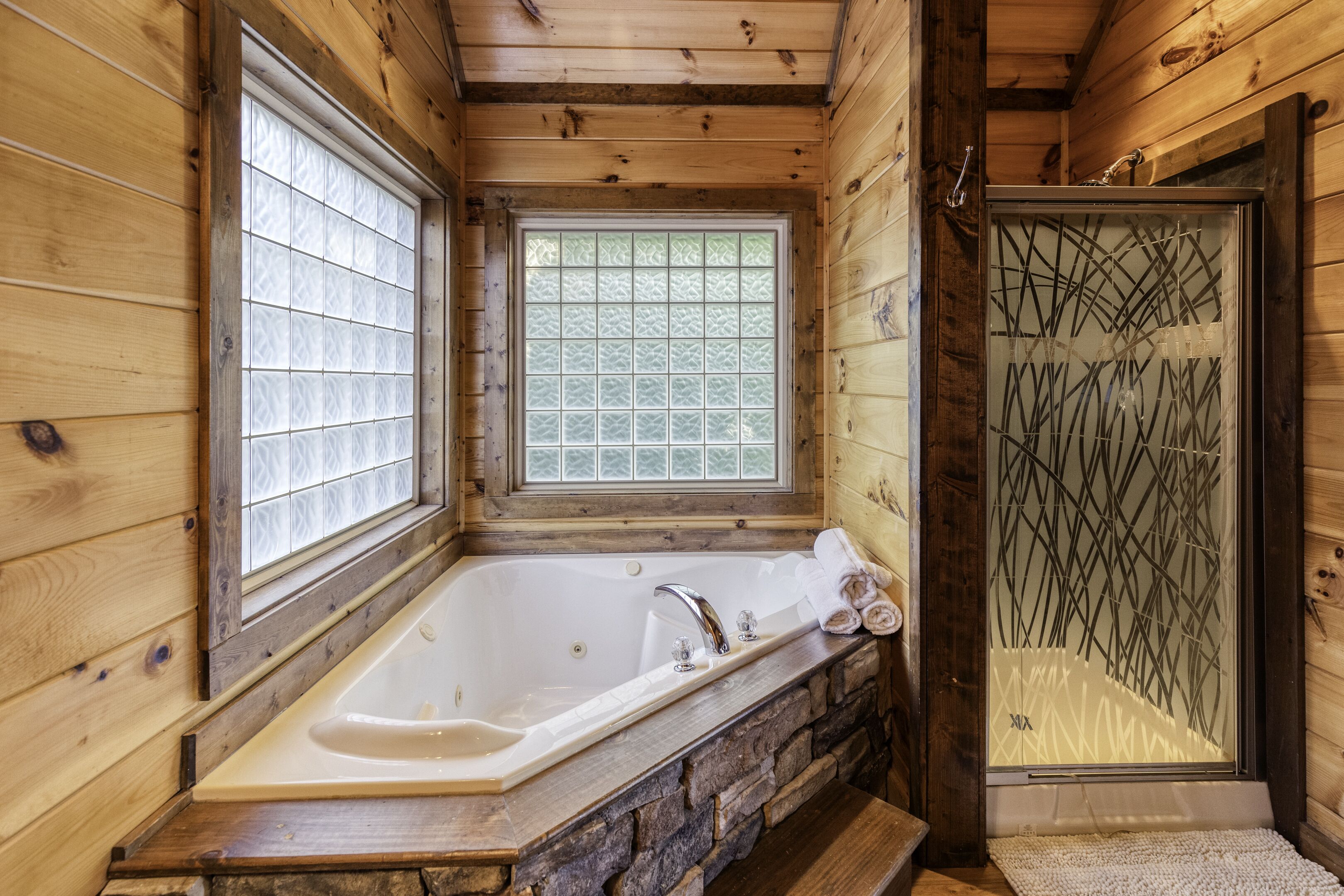 A wooden cabin bathroom with a stone sink, a bathtub, and a shower with a decorative glass door.