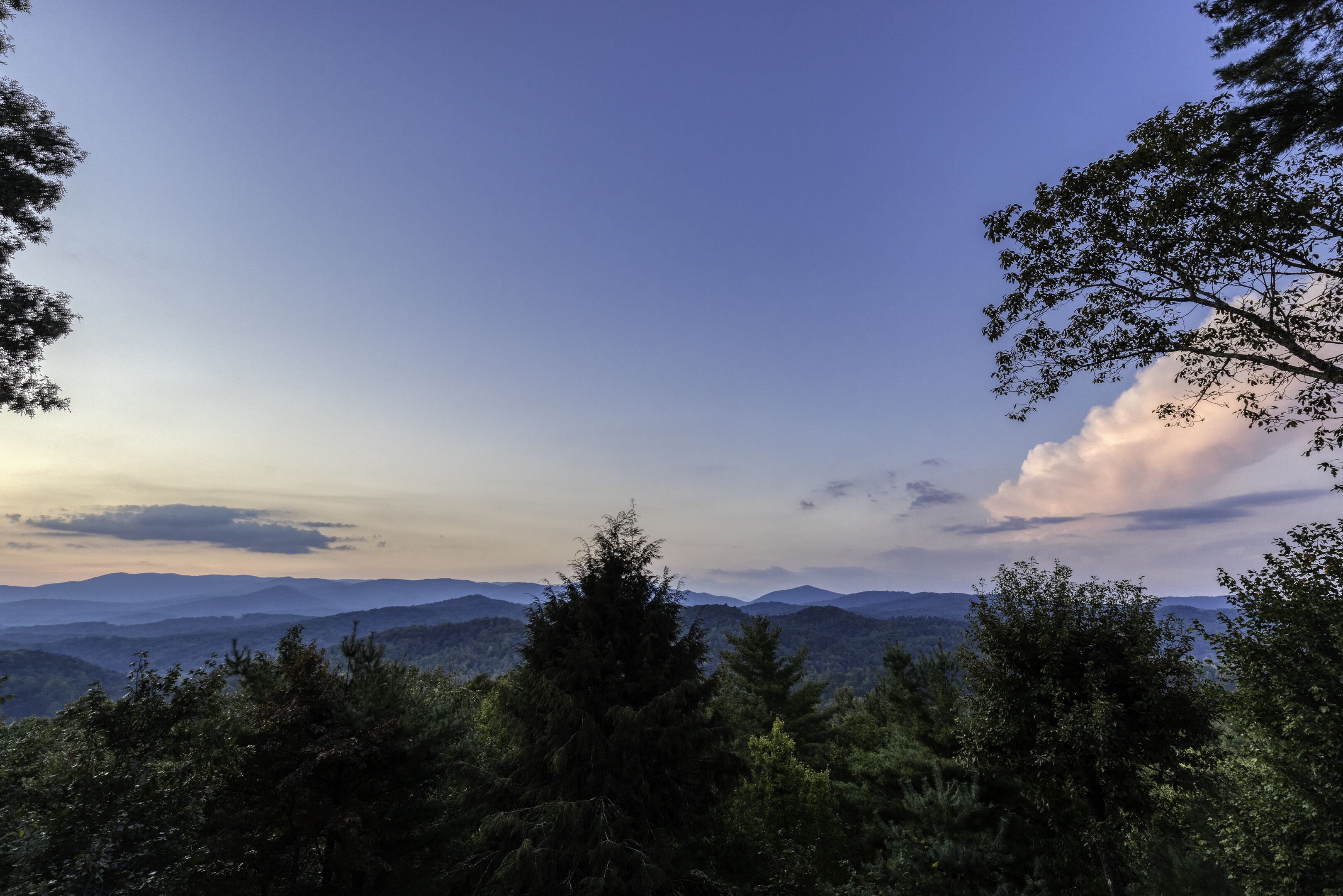 A mountainous landscape with dense forest in the foreground and distant hills under a clear sky.
