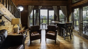 Un interior de madera con una escalera de madera, sillones de cuero, una mesa y ventanas amplias que ofrecen vistas al exterior.