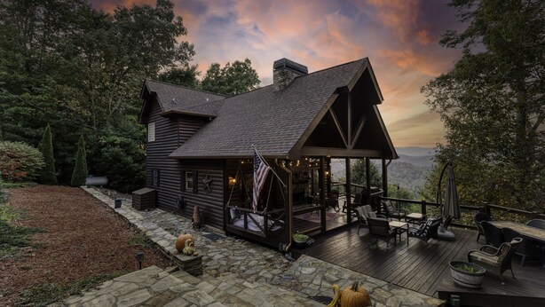 Una cabaña de madera con terraza, mobiliario exterior y vistas panorámicas a la montaña.