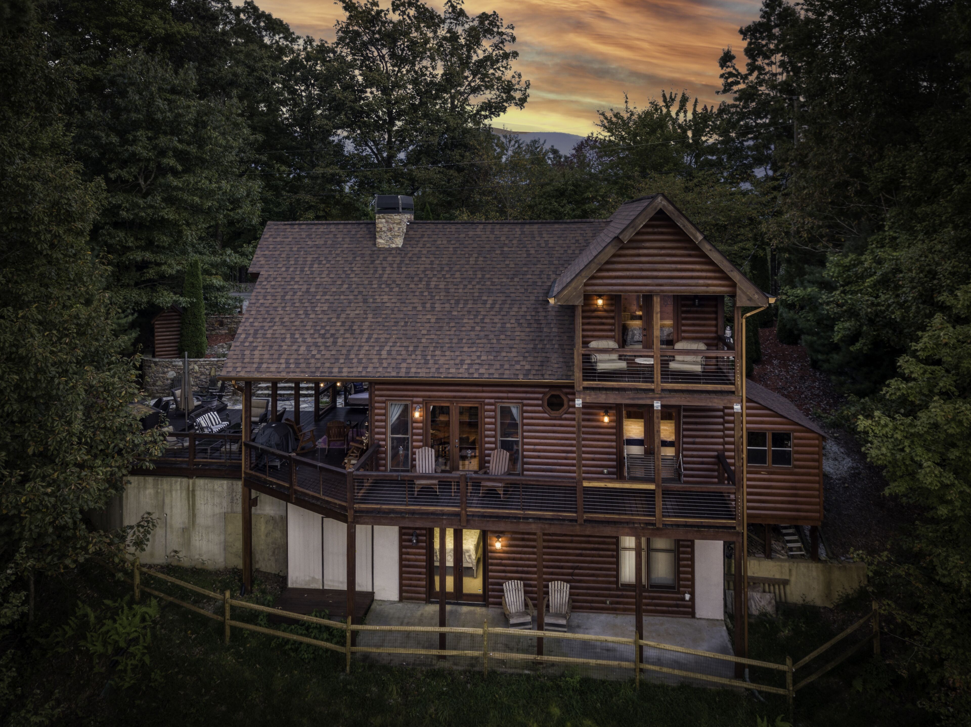 A two-story log cabin with a balcony and a deck, surrounded by trees.