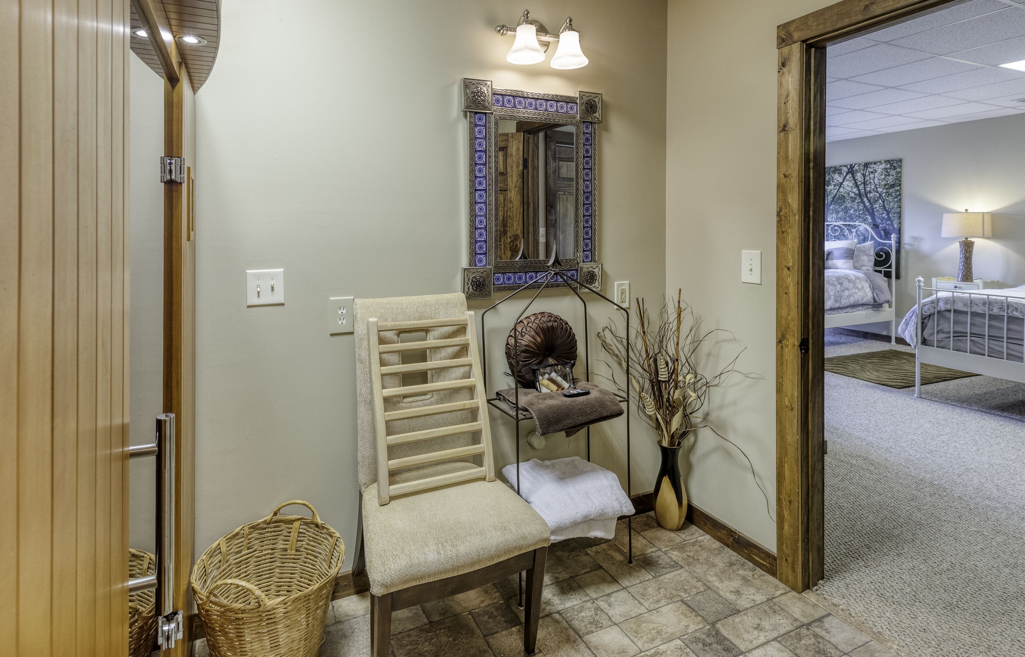 A hallway with a chair, a small table with a vase, and a mirror with decorative tiles.