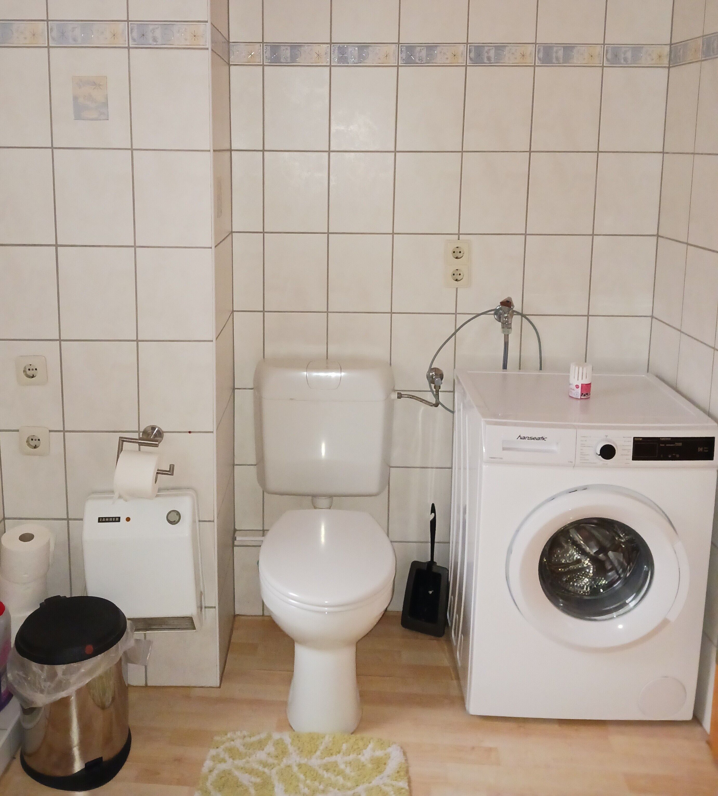 A bathroom with a toilet, a washing machine, and a trash bin.