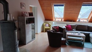 A loft-style room with a wooden ceiling, a built-in stove, a sofa, a chair, and a small table. - Holiday Apartment "Gersch" with Balcony & Wi-Fi (Traben-Trarbach/Wolf)