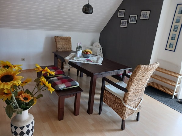 Un coin repas avec une table en bois, des chaises en osier, un vase rempli de tournesols et un mur orné de tableaux.
