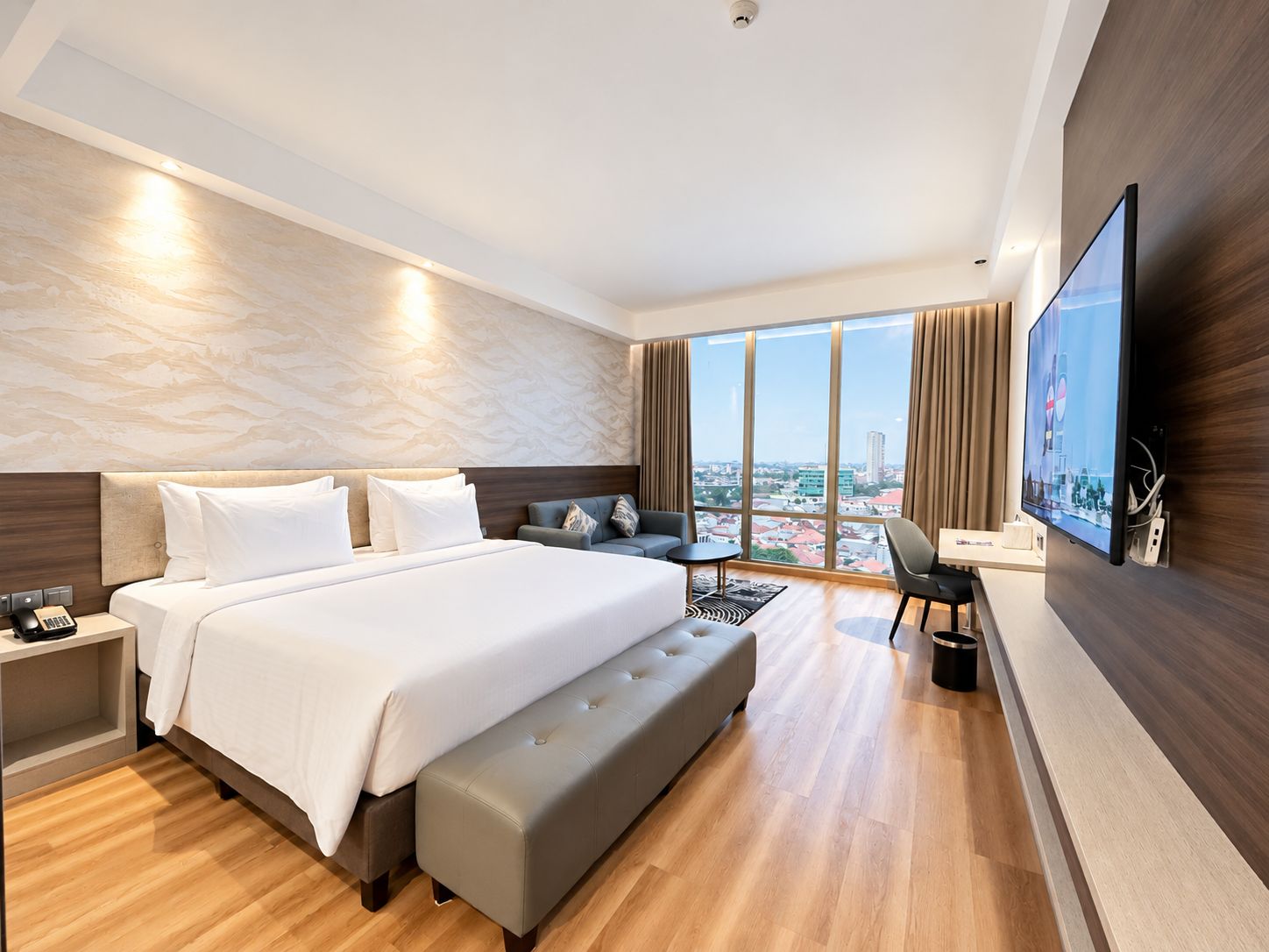 Una habitación de hotel moderna con una cama grande, una zona de estar, un televisor de pantalla plana y vistas a la ciudad.