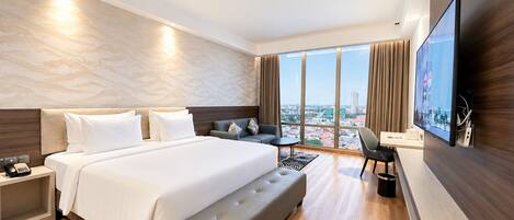 Una habitación de hotel moderna con una cama grande, una zona de estar, un televisor de pantalla plana y vistas a la ciudad.