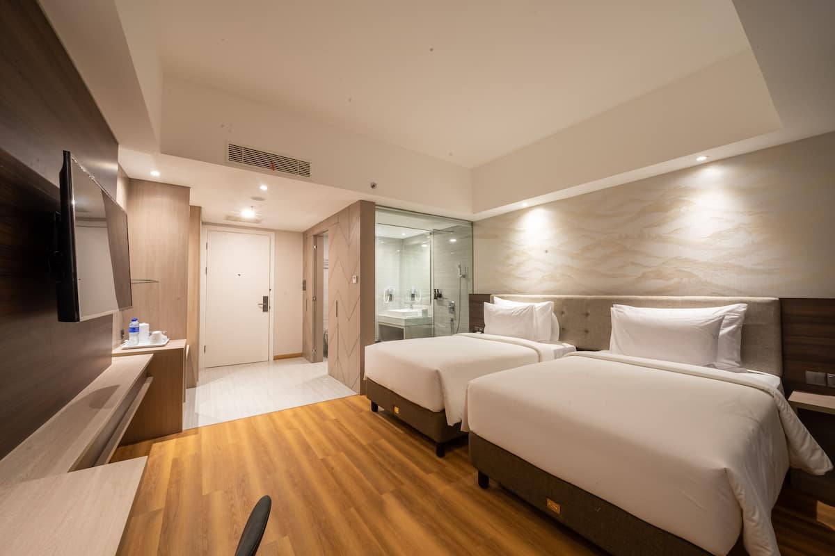 Een hotelkamer met twee bedden, een televisie, een bureau, een spiegel en een badkamer met douche en wastafel.