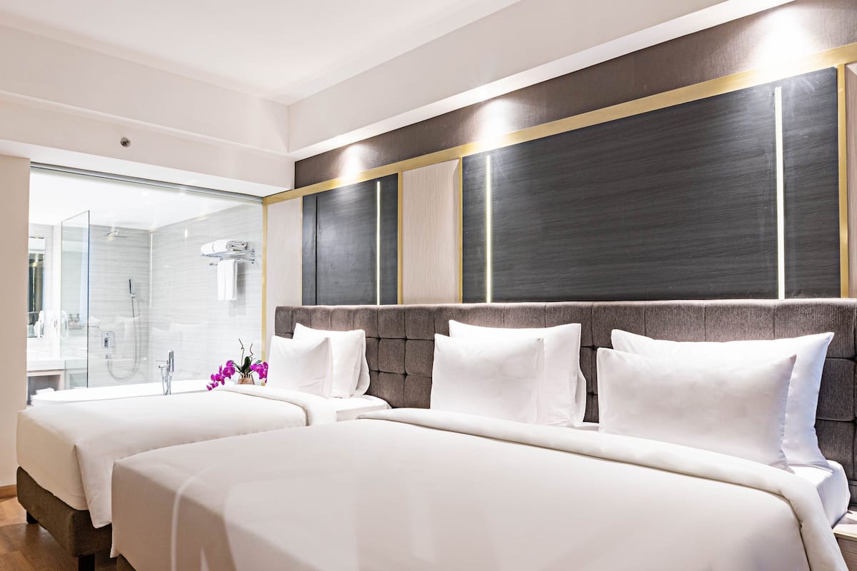 Een hotelkamer met twee bedden, een grote spiegel en een douchecabine met glazen wanden.