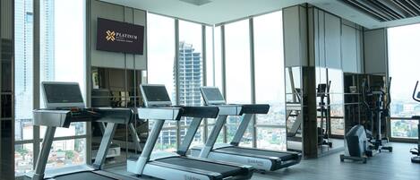A modern gym with treadmills, exercise equipment, and large windows offering city views.