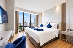A modern hotel room with a large bed, a desk, and a view of the city.