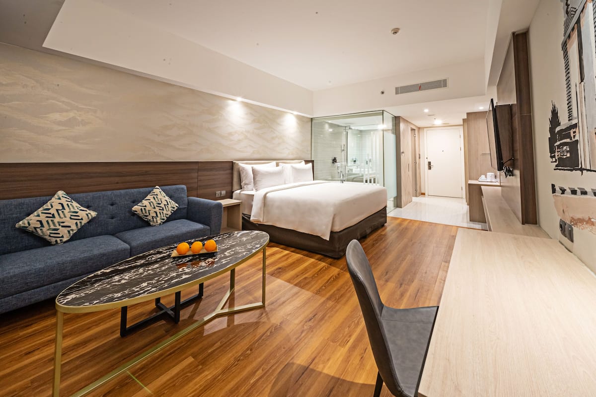 Een moderne hotelkamer met een bed, een bank, een glazen douchecabine en een zithoek.