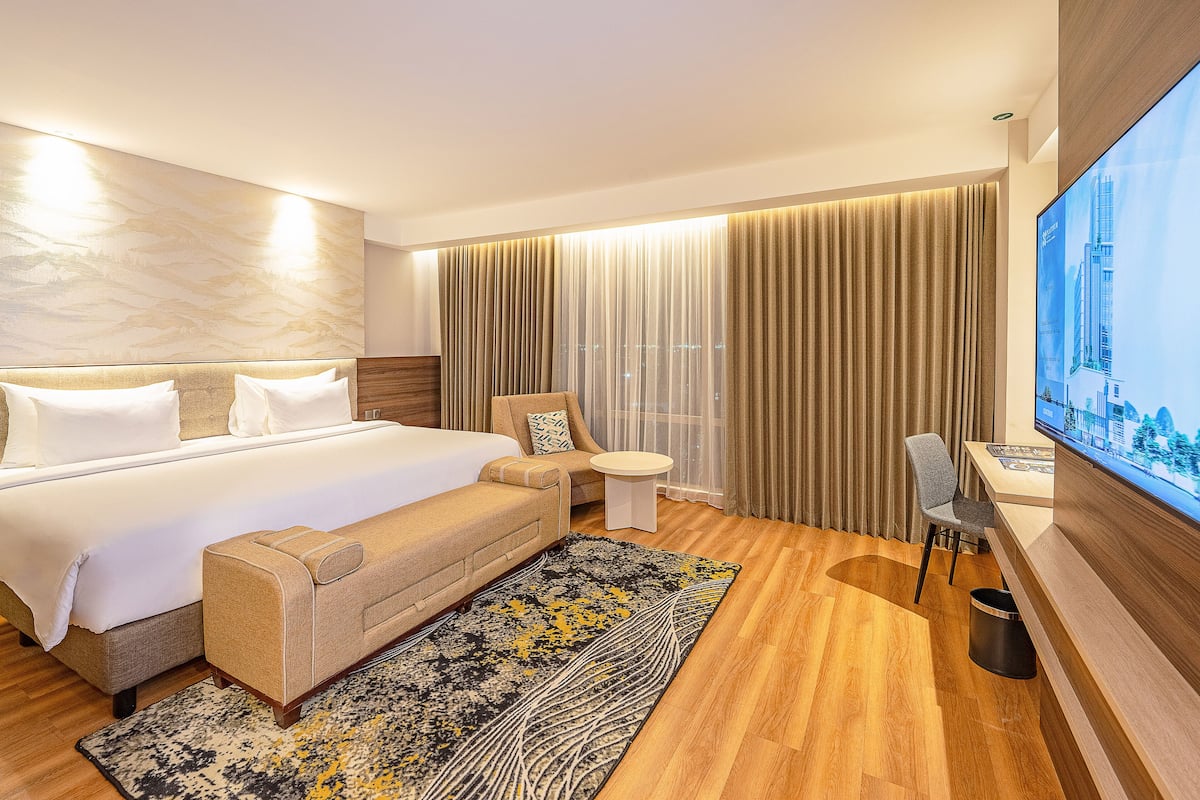 Een hotelkamer met een groot bed, een slaapbank, een tafeltje, een televisie en uitzicht op een stadsbeeld.