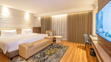 Habitación de hotel con una cama grande, un sofá, una mesita, un televisor y vistas a la ciudad.