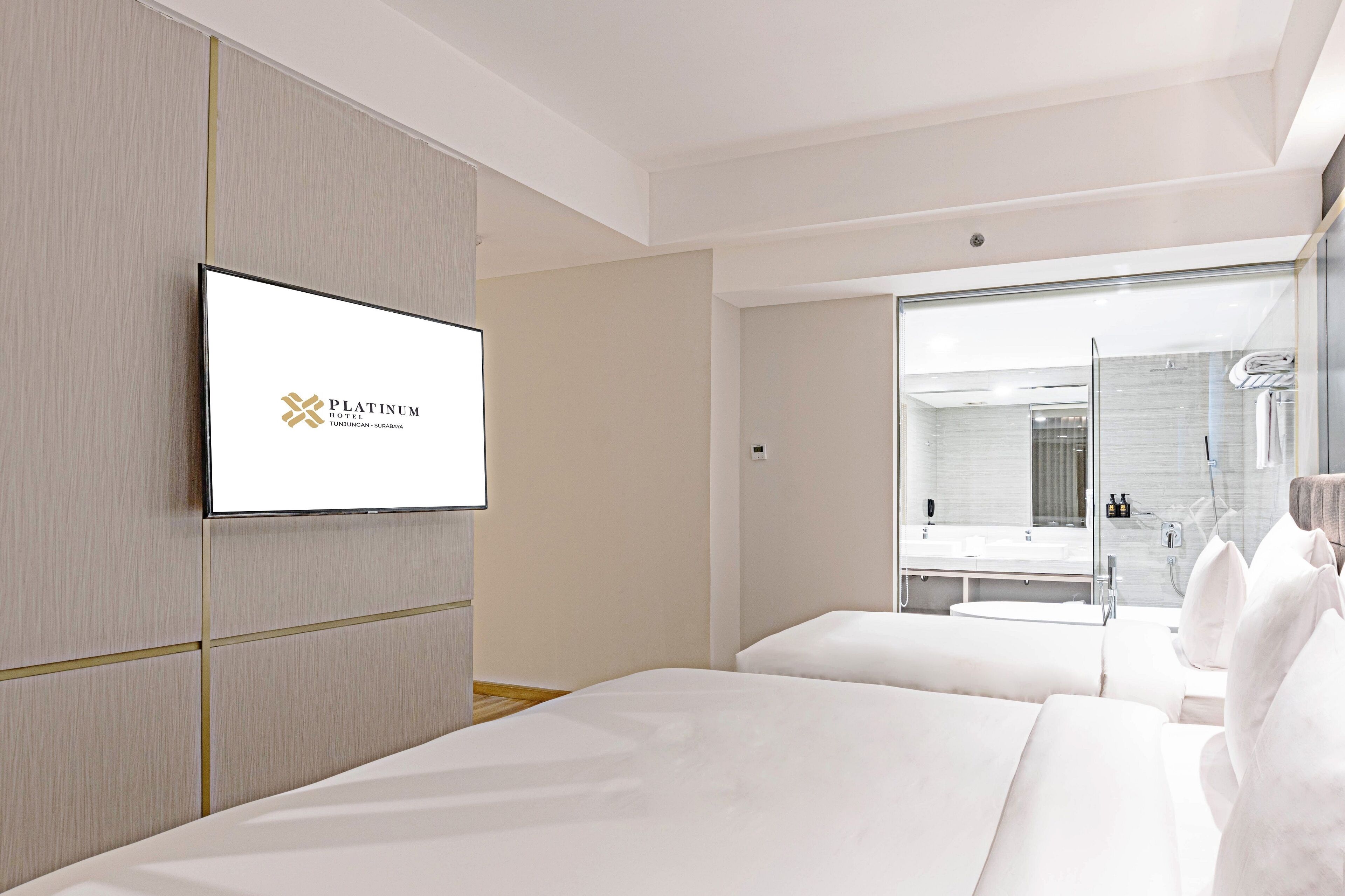 Una habitación de hotel moderna con una cama grande, un televisor montado en la pared y un baño con cabina de ducha de vidrio.