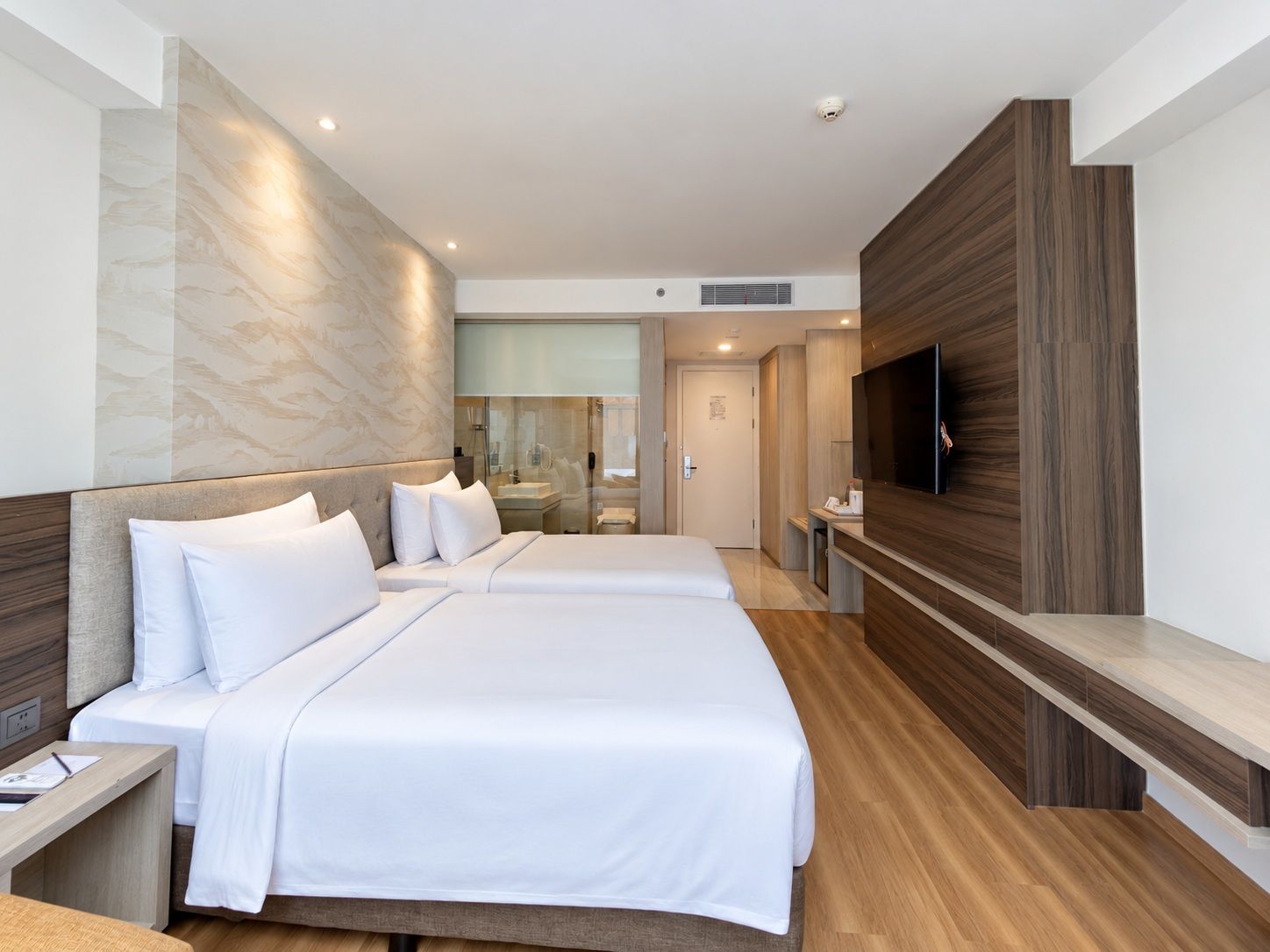 Habitación de hotel moderna con dos camas, televisión y baño con cabina de ducha de vidrio.
