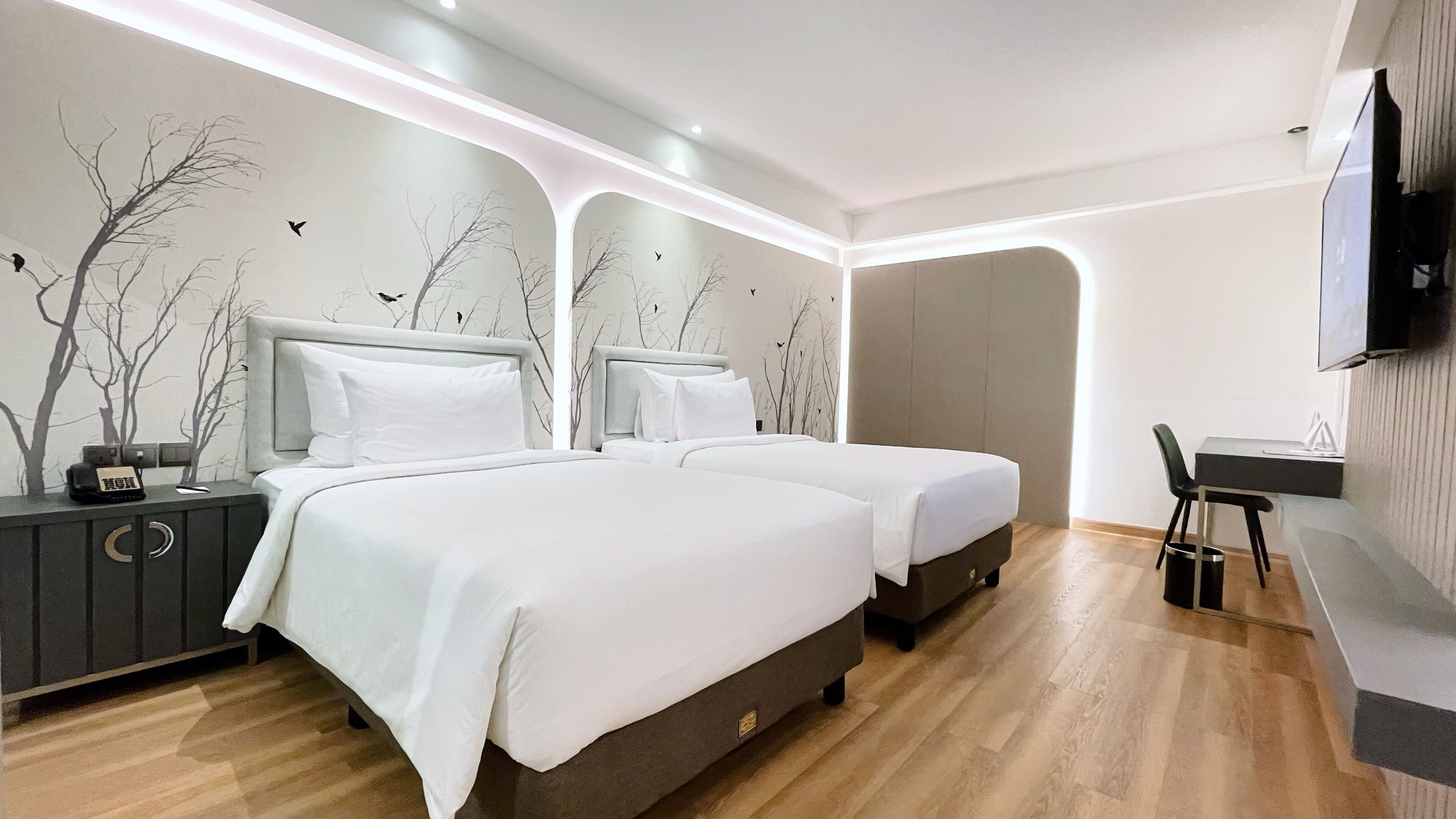 A modern hotel room with two beds, a desk, and a TV.