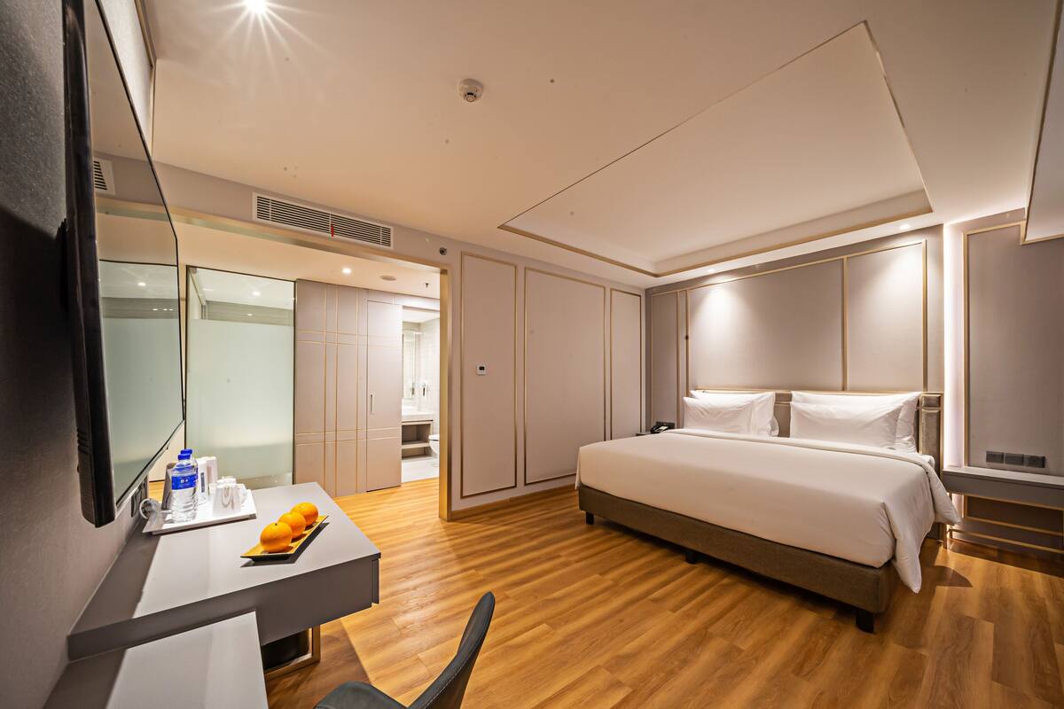 Een moderne hotelkamer met een groot bed, een bureau met stoel, een spiegel en een badkamer die door een geopende deur zichtbaar is.