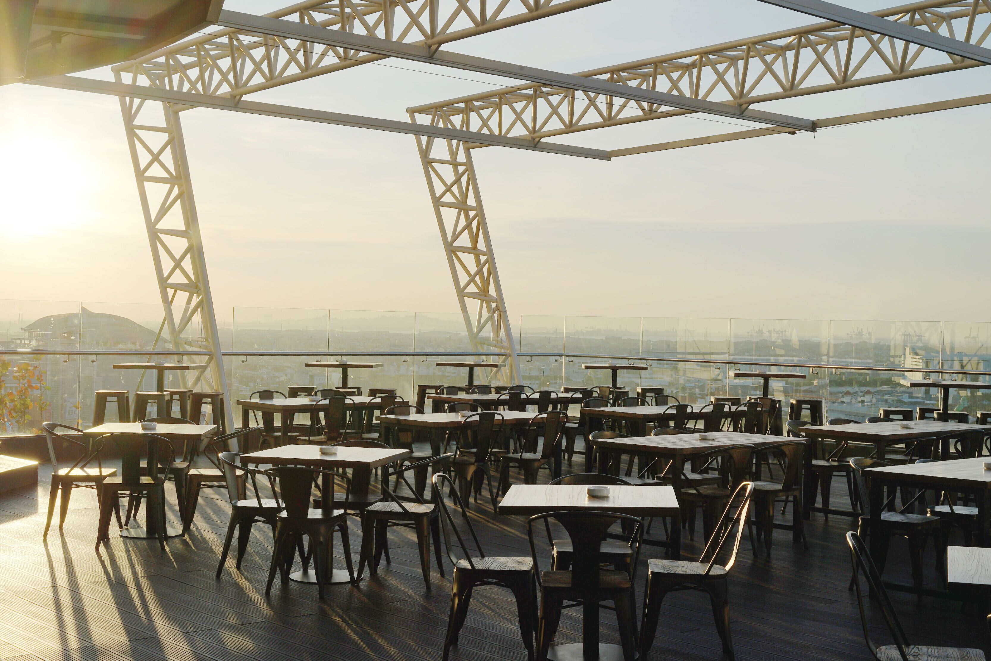 An outdoor dining area with tables and chairs, large windows, and a view of the cityscape.