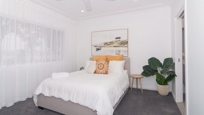 A bedroom with a bed, a small side table, a potted plant, and a window with sheer curtains. - Charming 3 bedroom, modern, waterfront home (North Haven)