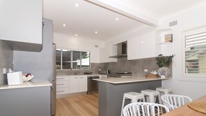 A modern kitchen with white cabinetry, a central island, and a dining area with white chairs. - Charming 3 bedroom, modern, waterfront home (North Haven)