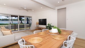 A modern dining area with a wooden table, white chairs, and a TV on the wall. - Charming 3 bedroom, modern, waterfront home (North Haven)