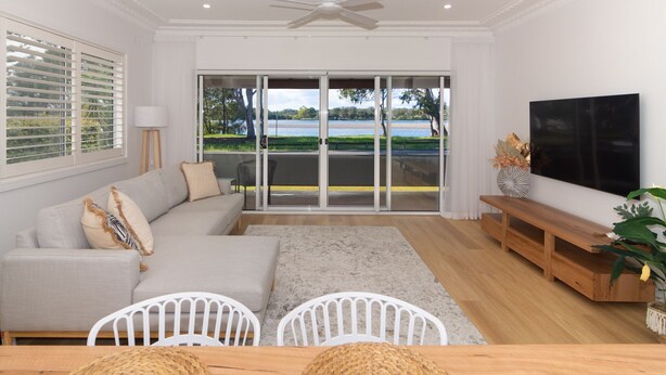 A modern living room with a grey sectional sofa, a wooden bench, and a TV. - Charming 3 bedroom, modern, waterfront home (North Haven)
