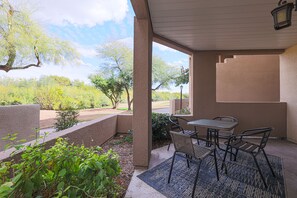 An outdoor patio with a table and chairs, surrounded by plants and a view of a landscaped area with trees and a pathway. - Scottsdale ground floor golf course condo (Scottsdale)