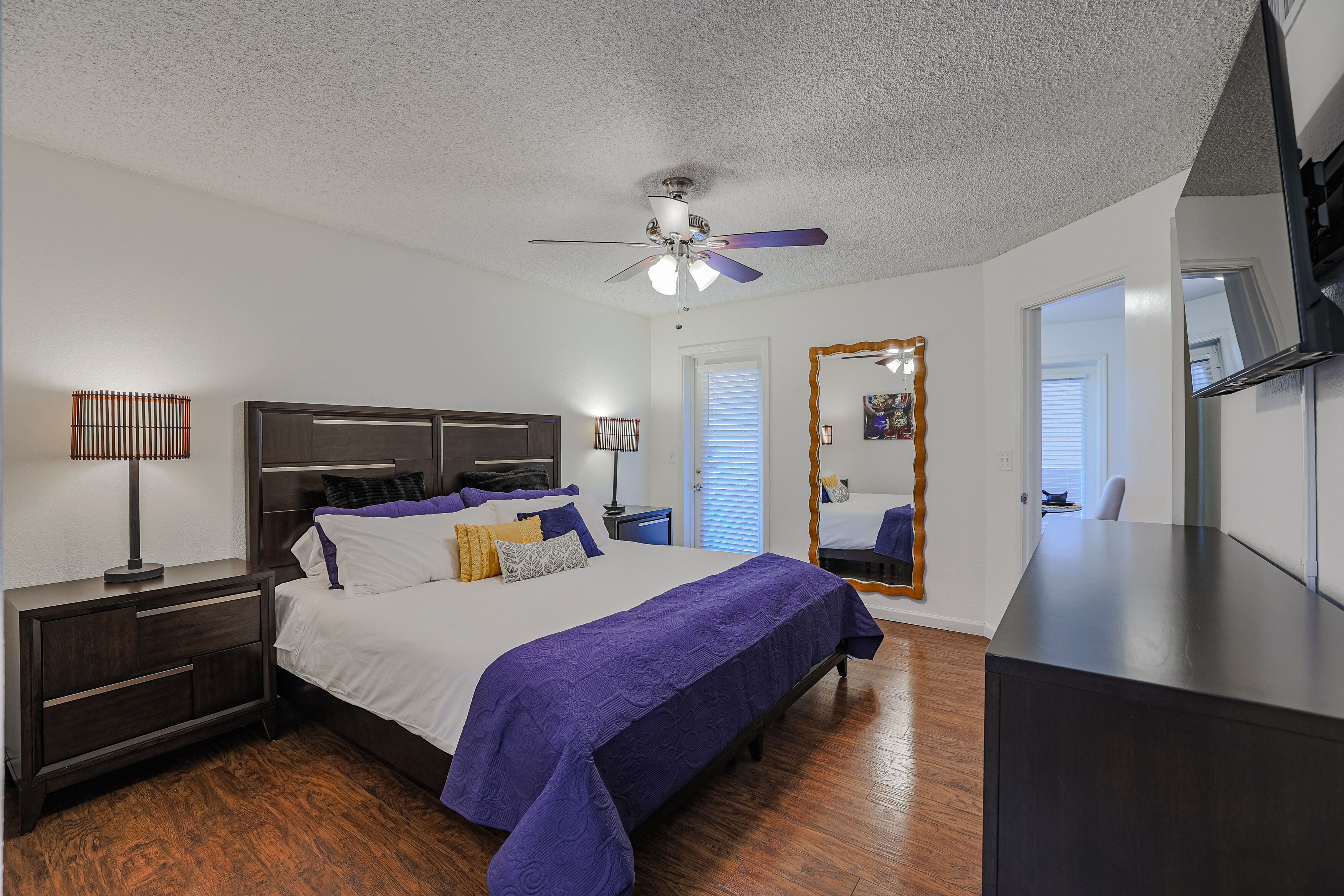Une chambre à coucher comprenant un lit, des tables de chevet, un ventilateur de plafond, une commode et un miroir.