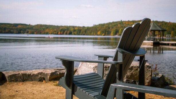 Een Adirondack stoel aan een meer, met een prieel op de achtergrond.