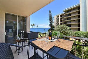 A balcony with a table set for two, overlooking a body of water and a building with multiple balconies.