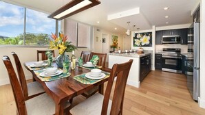 A modern kitchen with stainless steel appliances, a dining area with wooden furniture, and a view of the outdoors. - Royal Kahana 301 Remodeled OceanFront 2BD w Ocean Views Pool (Lahaina)