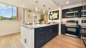 A modern kitchen with dark cabinets, stainless steel appliances, and a large island with a marble countertop. - Royal Kahana 301 Remodeled OceanFront 2BD w Ocean Views Pool (Lahaina)