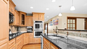 Una cocina con armarios de madera, electrodomésticos de acero inoxidable, encimera de granito e iluminación empotrada.