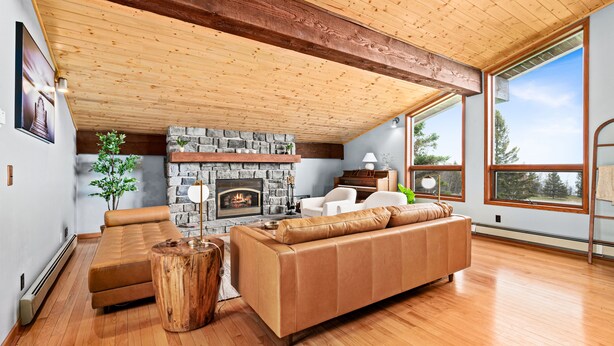 Amplia sala de estar con chimenea de piedra, vigas de techo de madera y grandes ventanas que ofrecen vistas al exterior.