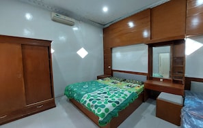 A bedroom with a wooden wardrobe, a bed with patterned bedding, a bedside table, and a mirror. - ARJUNA HOMESTAY (Srimulyo)